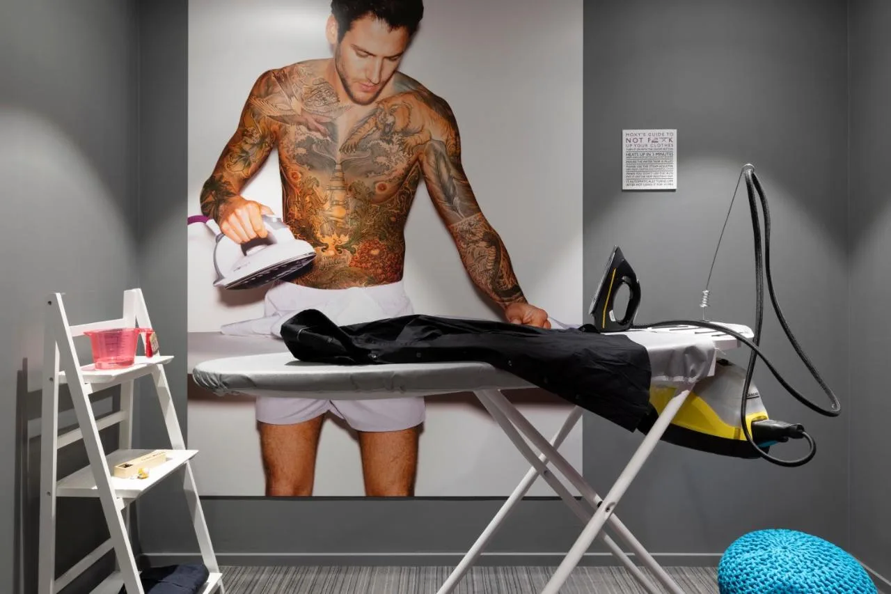 a man with tattoos standing next to a bed at Moxy Glasgow Merchant City in Glasgow